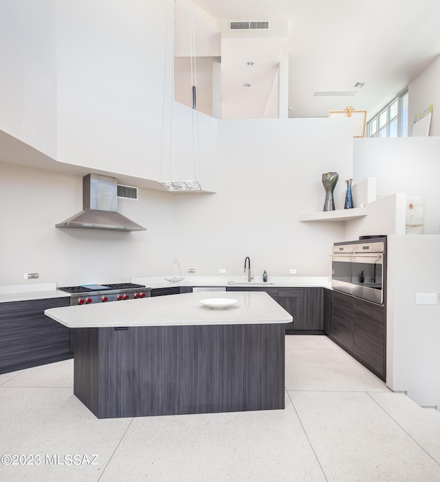 kitchen with dark brown cabinetry, sink, a center island, wall chimney range hood, and appliances with stainless steel finishes