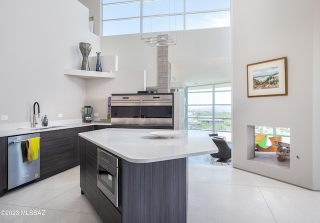 kitchen with a center island, a high ceiling, sink, appliances with stainless steel finishes, and dark brown cabinets