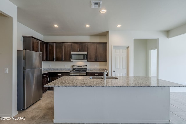 kitchen featuring a kitchen island with sink, sink, light stone countertops, and appliances with stainless steel finishes