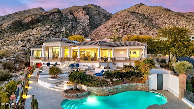 back house at dusk with a mountain view and a patio area