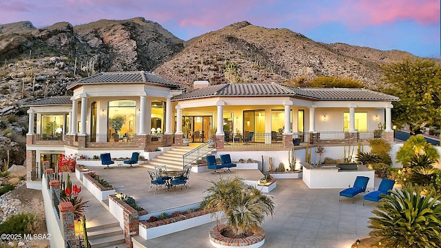 back house at dusk with an outdoor kitchen, a mountain view, an outdoor bar, and a patio