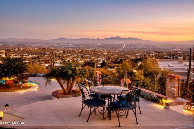 patio terrace at dusk with a mountain view and a fenced in pool