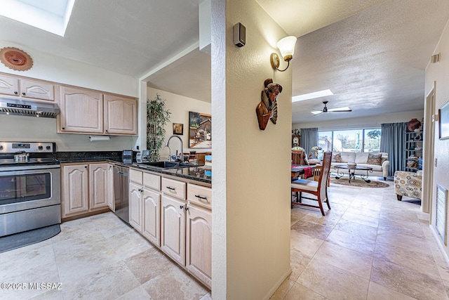 kitchen with a skylight, a sink, stainless steel appliances, under cabinet range hood, and dark countertops