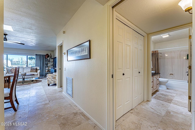 hallway with visible vents, a textured ceiling, baseboards, and a textured wall