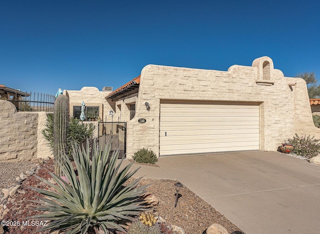 adobe home featuring fence, a garage, driveway, and stucco siding