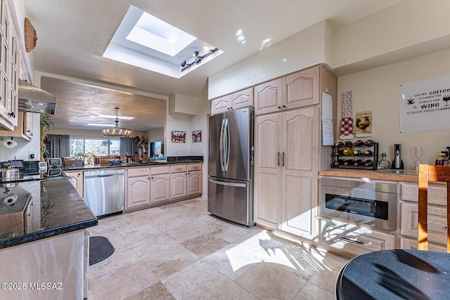 kitchen featuring range hood, light brown cabinets, an inviting chandelier, a skylight, and appliances with stainless steel finishes