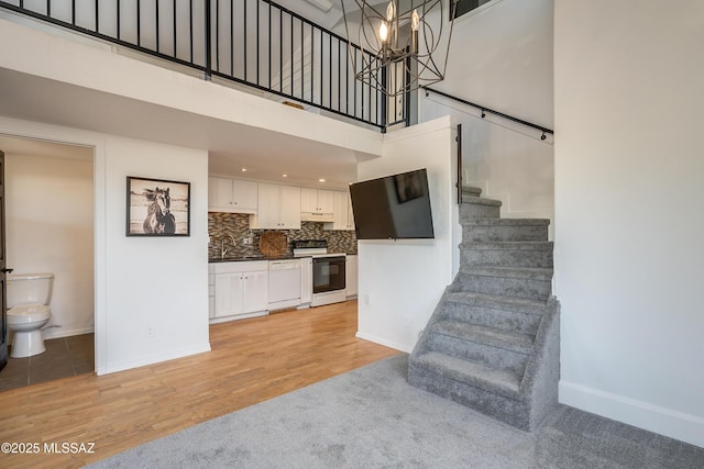 stairs featuring baseboards, wood finished floors, a towering ceiling, and a notable chandelier