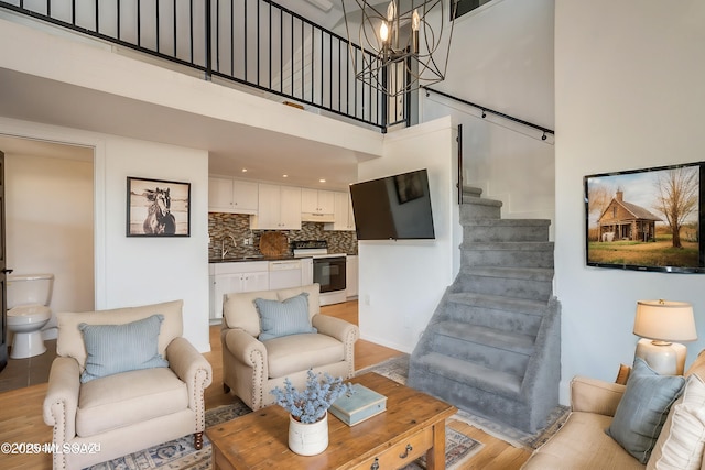 living room with stairs, light wood finished floors, a towering ceiling, and a notable chandelier