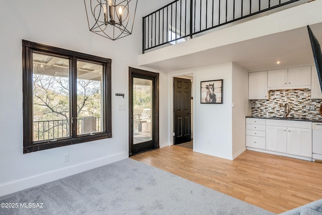 entryway with a towering ceiling, light wood finished floors, baseboards, and a chandelier