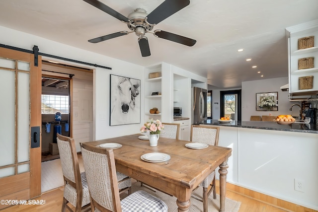 dining space with recessed lighting, light wood-style flooring, a ceiling fan, and a barn door