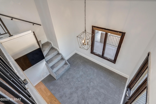 staircase featuring baseboards, a chandelier, and carpet flooring