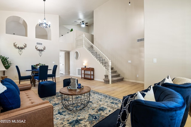 living room with wood-type flooring, ceiling fan with notable chandelier, and a high ceiling