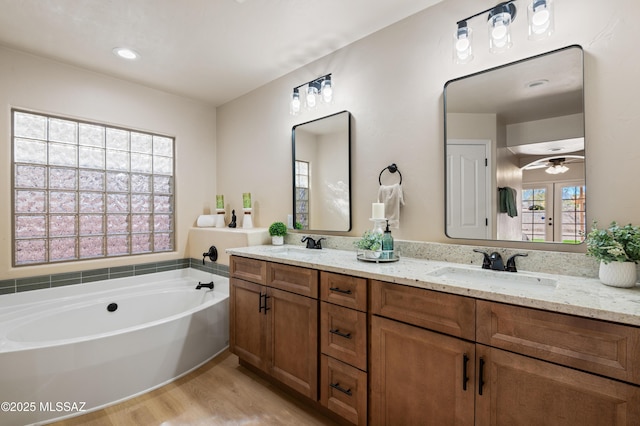 bathroom featuring ceiling fan, french doors, a bath, hardwood / wood-style floors, and vanity