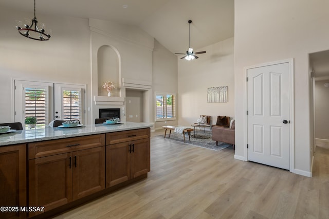 kitchen featuring high vaulted ceiling, french doors, ceiling fan, light hardwood / wood-style floors, and light stone counters