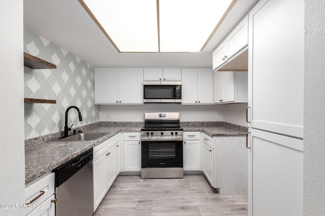 kitchen featuring light wood-type flooring, dark stone counters, stainless steel appliances, sink, and white cabinets