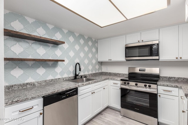 kitchen featuring white cabinets, sink, light wood-type flooring, appliances with stainless steel finishes, and light stone counters