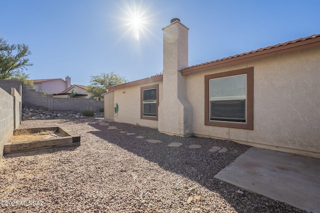 rear view of property with a chimney, fence, and stucco siding