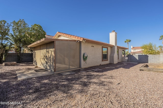 back of property featuring a tile roof, a fenced backyard, a chimney, and stucco siding