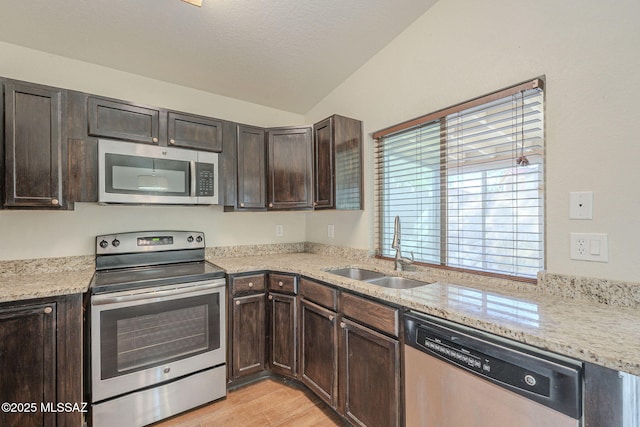 kitchen with stainless steel appliances, light wood-type flooring, lofted ceiling, dark brown cabinetry, and sink