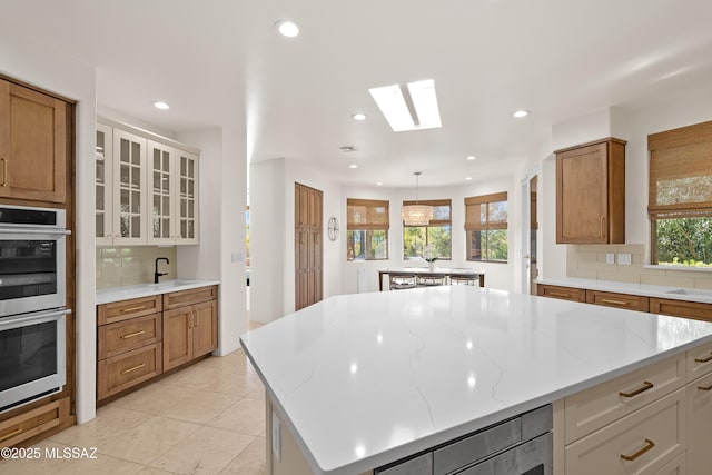 kitchen featuring a center island, double oven, light stone counters, decorative backsplash, and a sink