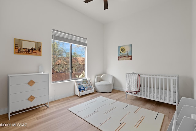 bedroom with baseboards, a ceiling fan, a nursery area, and wood finished floors