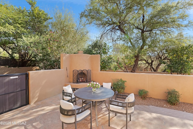 view of patio with exterior fireplace, outdoor dining area, and fence