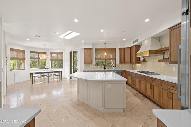 kitchen featuring custom exhaust hood, decorative backsplash, brown cabinets, and appliances with stainless steel finishes