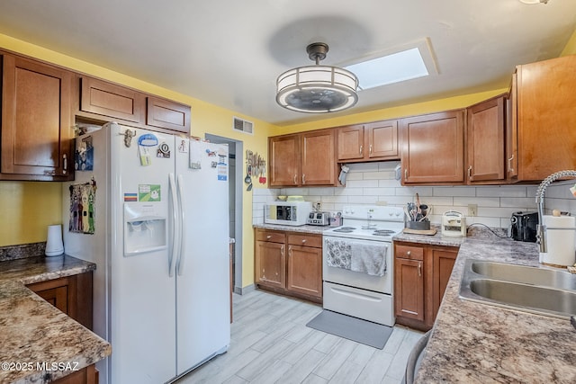 kitchen featuring white appliances, sink, a skylight, light stone countertops, and tasteful backsplash