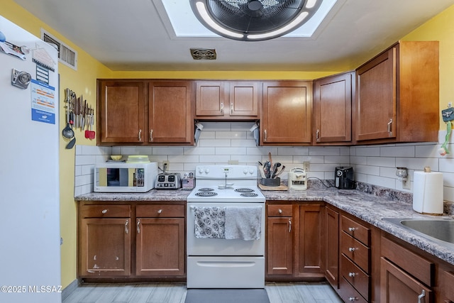 kitchen with tasteful backsplash, light stone counters, white appliances, and light wood-type flooring