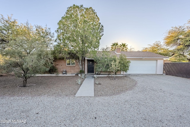 ranch-style home featuring gravel driveway, brick siding, a chimney, an attached garage, and fence