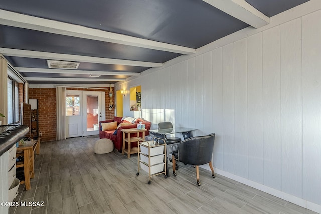 interior space featuring beamed ceiling, hardwood / wood-style floors, brick wall, and french doors