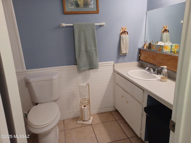 half bathroom with tile patterned flooring, toilet, vanity, and a wainscoted wall