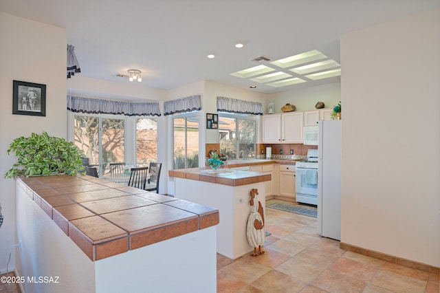 kitchen with a skylight, tile counters, white appliances, white cabinets, and a center island