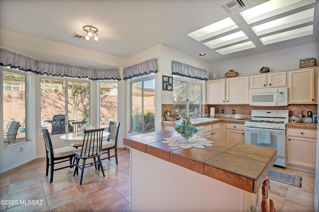 kitchen featuring backsplash, tile countertops, sink, white appliances, and a skylight