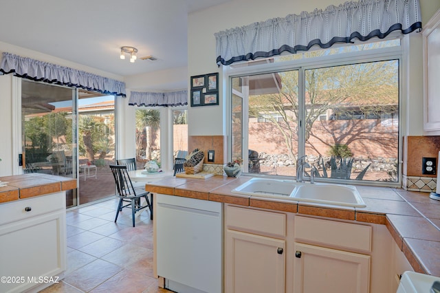 kitchen with white dishwasher, sink, white cabinets, and tile counters