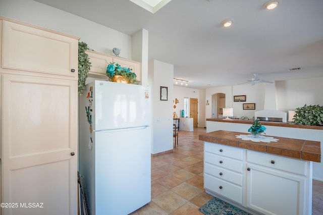 kitchen featuring ceiling fan, tile countertops, white refrigerator, and cream cabinets