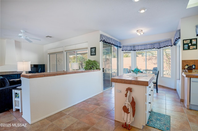 kitchen featuring dishwashing machine, a kitchen island, white cabinetry, tile countertops, and ceiling fan