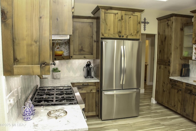 kitchen featuring decorative backsplash, light stone countertops, light wood-type flooring, and appliances with stainless steel finishes