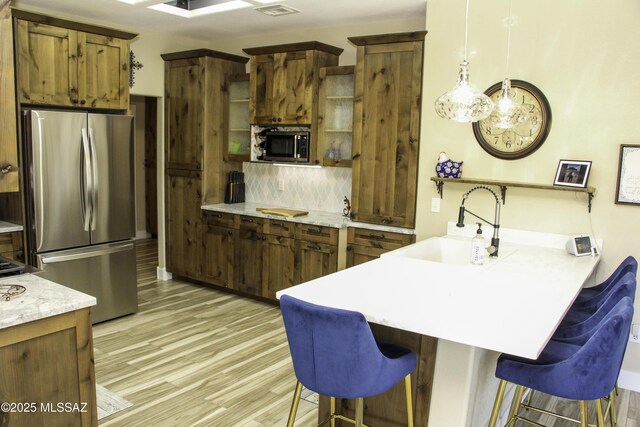 kitchen featuring pendant lighting, a kitchen breakfast bar, sink, kitchen peninsula, and stainless steel refrigerator