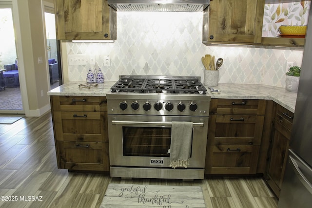 kitchen featuring tasteful backsplash, light stone counters, light hardwood / wood-style floors, extractor fan, and appliances with stainless steel finishes