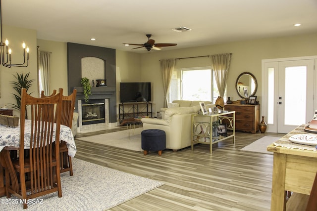 living room with a large fireplace, wood-type flooring, and ceiling fan with notable chandelier