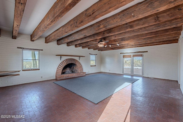 unfurnished living room with brick wall, a fireplace, beam ceiling, and brick floor