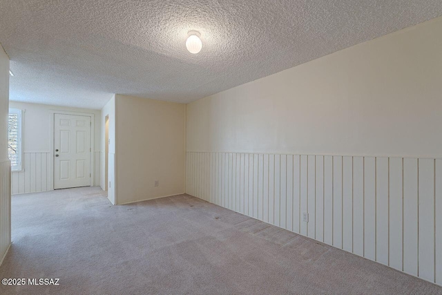 carpeted spare room with a textured ceiling and wainscoting