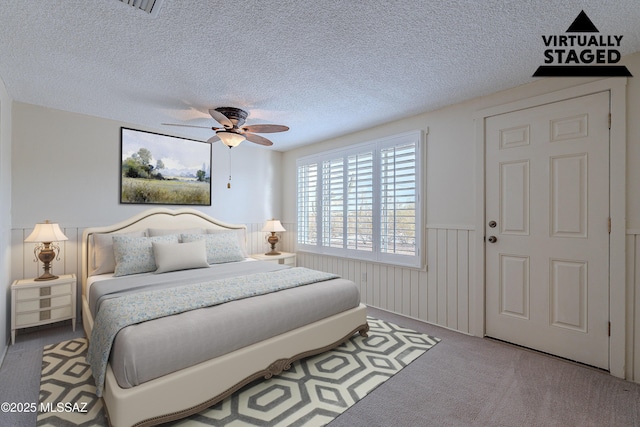 carpeted bedroom with a textured ceiling, ceiling fan, and wainscoting