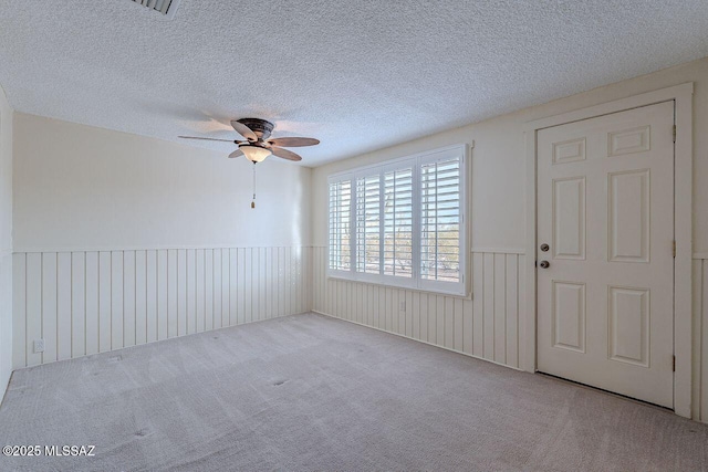 carpeted empty room featuring a ceiling fan, wainscoting, and a textured ceiling