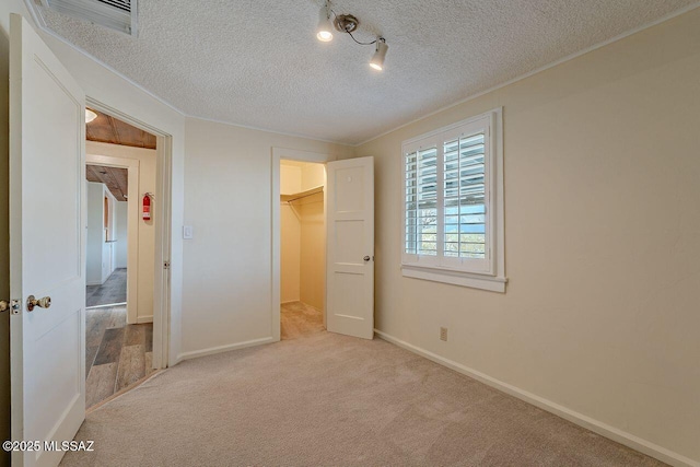 unfurnished bedroom featuring a textured ceiling, carpet floors, visible vents, baseboards, and a spacious closet