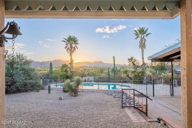 pool at dusk with fence, a patio, a community pool, and a mountain view