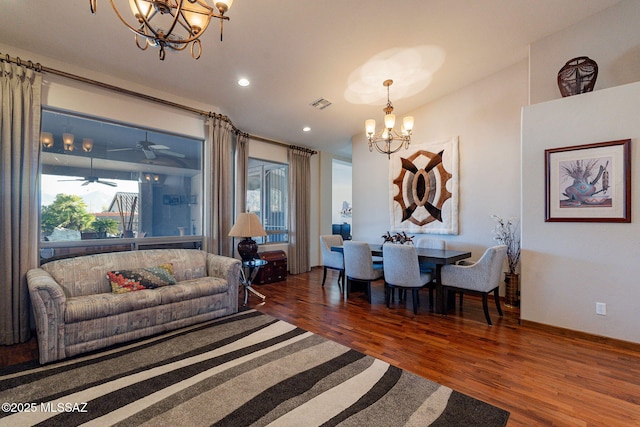 living room with ceiling fan with notable chandelier and dark hardwood / wood-style flooring