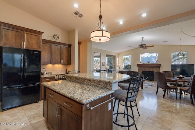 kitchen featuring ceiling fan, a kitchen breakfast bar, black fridge, vaulted ceiling, and a kitchen island