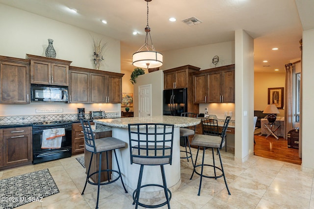 kitchen with a center island, a kitchen bar, black appliances, decorative light fixtures, and light stone counters